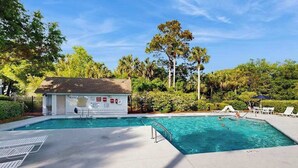 A swimming pool with a lifeguard station, lounge chairs, and a tropical garden setting.