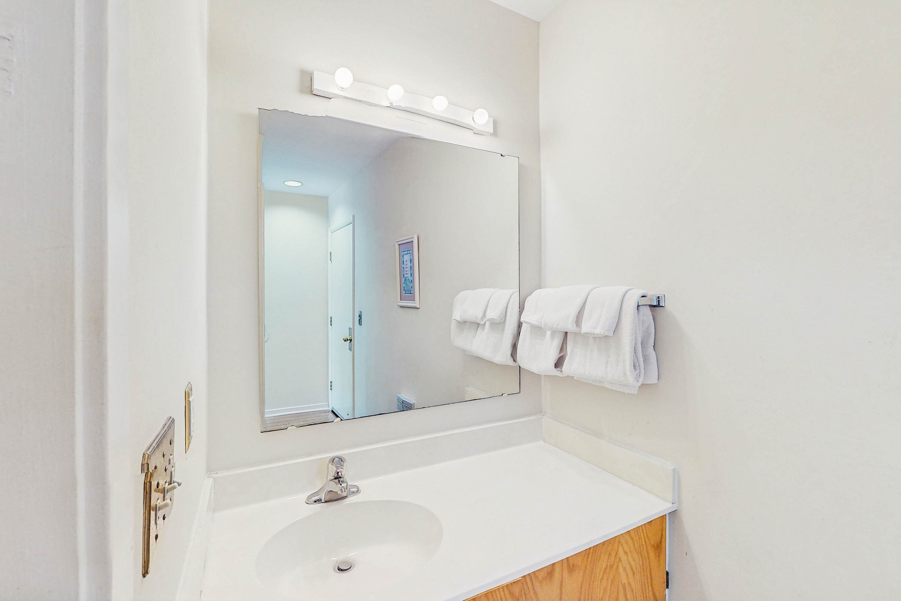 A bathroom with a white sink, a large mirror with lights, and a towel rack.