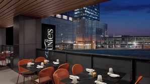 A rooftop dining area with tables set for four, orange chairs, and a city view at dusk. - Motto by Hilton Nashville Downtown (Nashville)