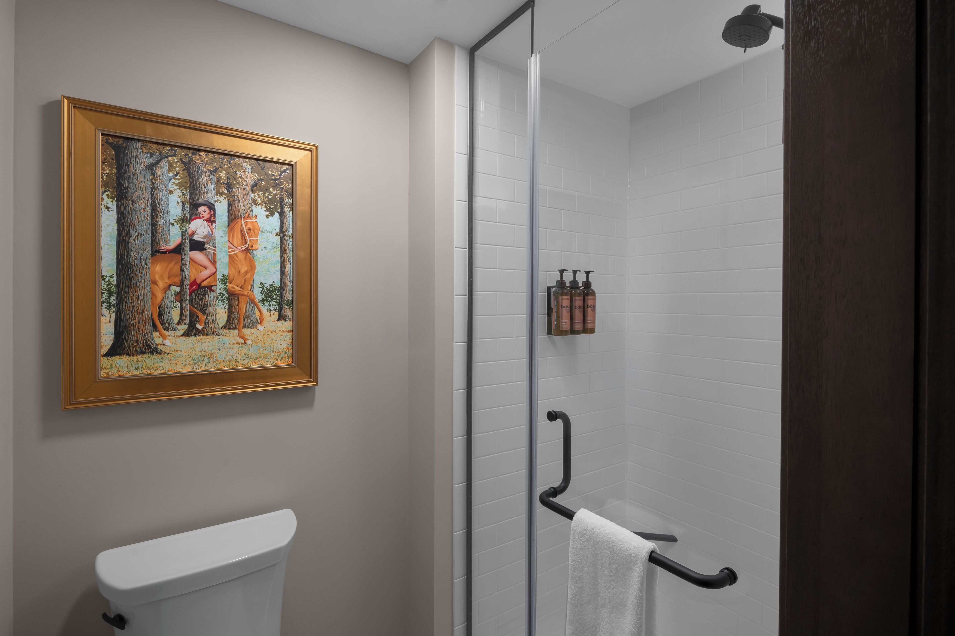 Un baño con inodoro, cabina de ducha de vidrio, toallero y un cuadro en la pared.