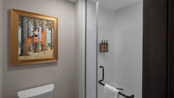 Un baño con inodoro, cabina de ducha de vidrio, toallero y un cuadro en la pared.