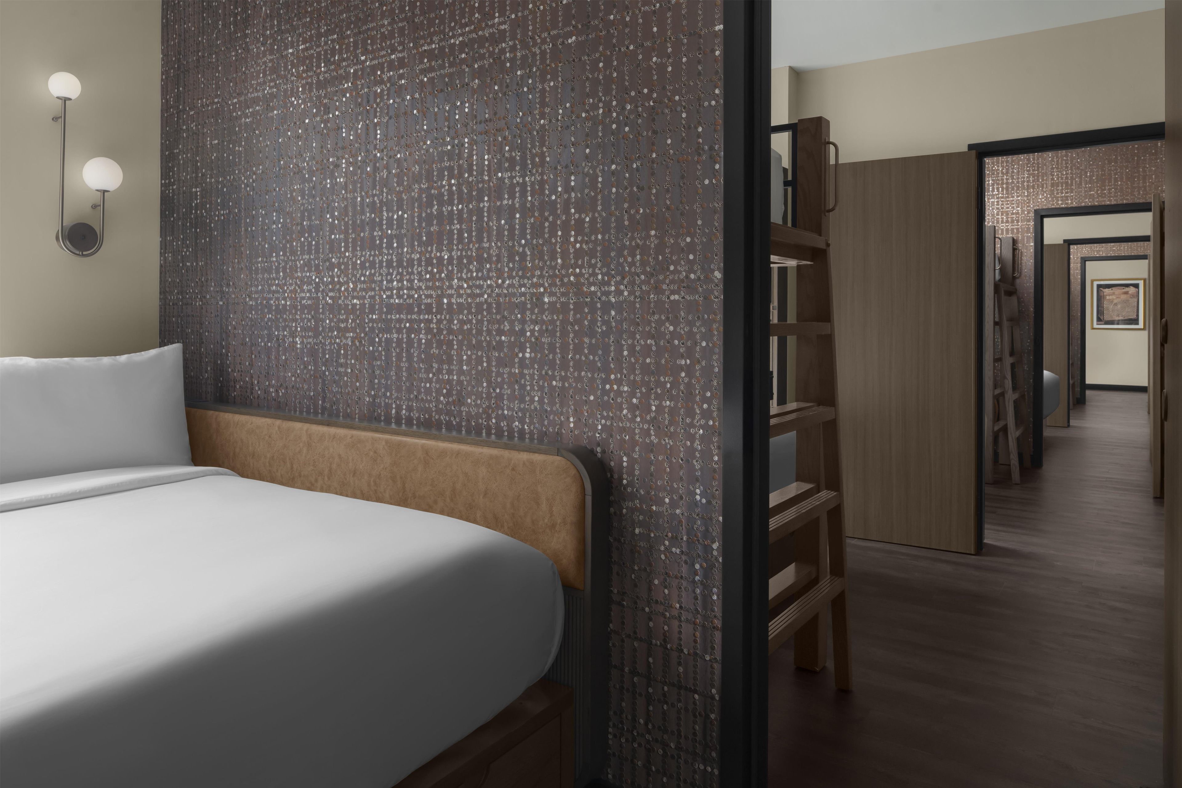 Una camera d'albergo con un letto, una parete decorata, una panca in legno e un corridoio che porta a un'altra stanza.