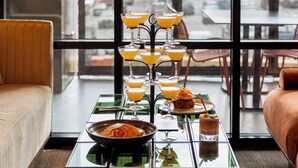 A modern dining area with a glass table set for a meal, a sofa, and a view of the city through large windows. - Motto by Hilton Nashville Downtown (Nashville)