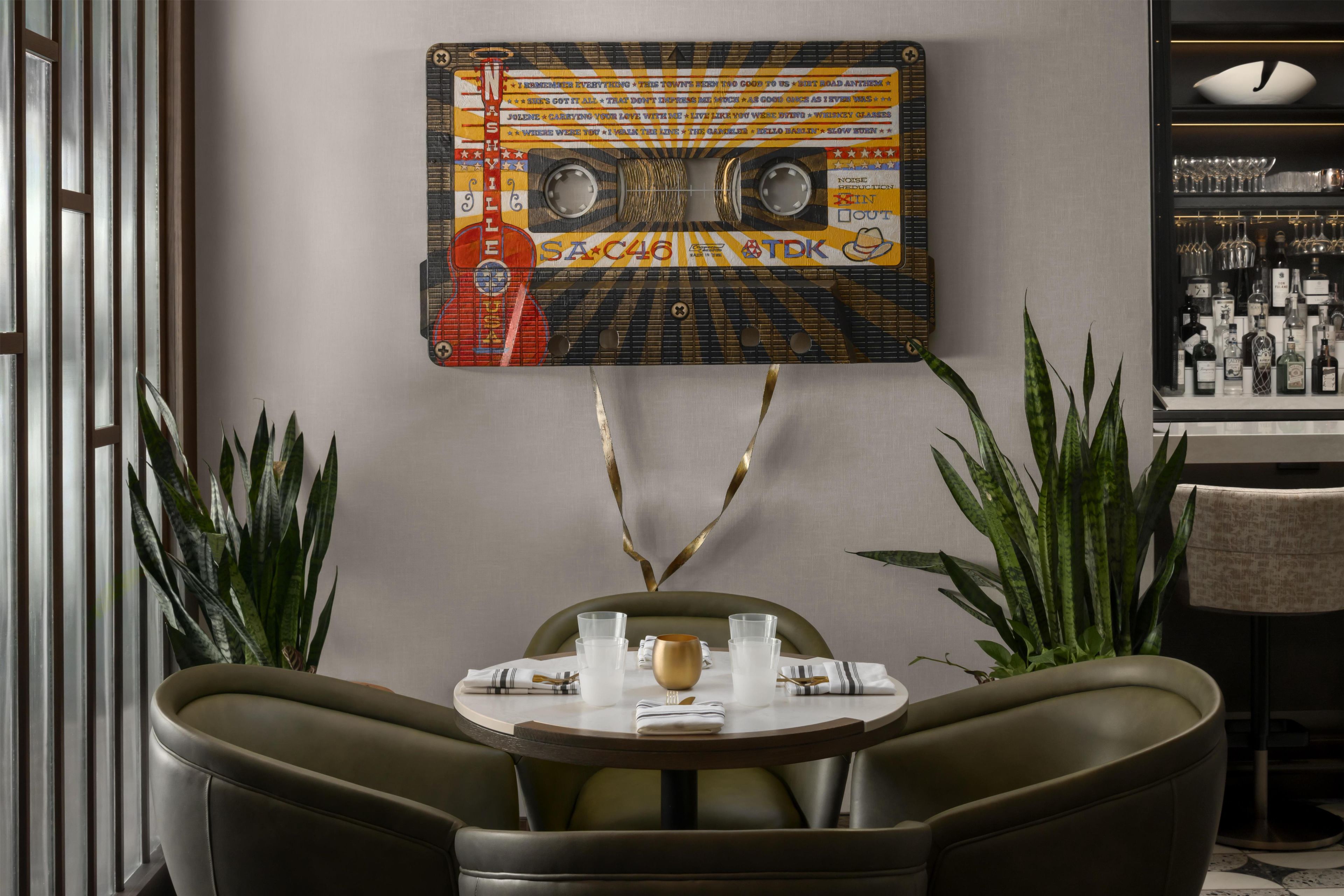 A dining area with a retro-themed wall art, a round table, two chairs, and a bar area with bottles.