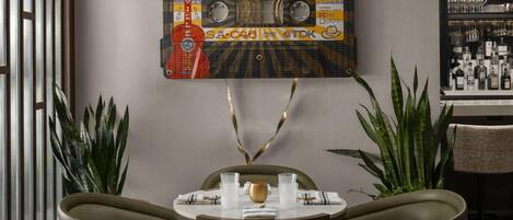 A dining area with a retro-themed wall art, a round table, two chairs, and a bar area with bottles.