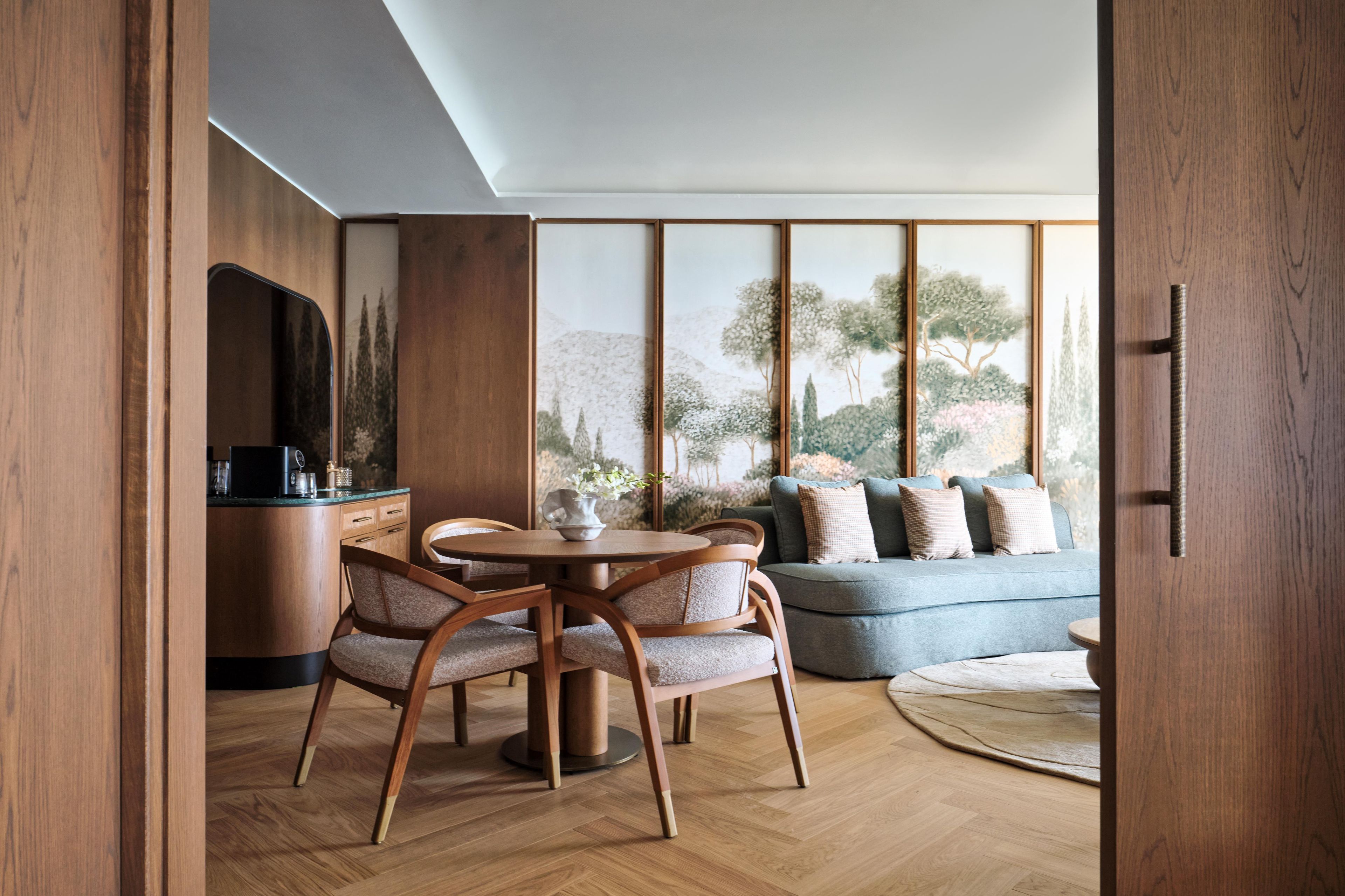 Un interior moderno con zona de comedor, sofá y vistas a árboles a través de amplios ventanales.