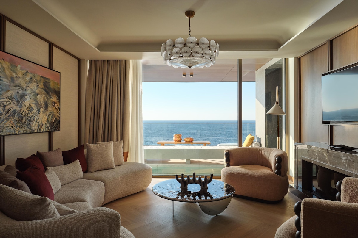 A modern living room with a large window, a chandelier, a sofa, a coffee table, and a television.
