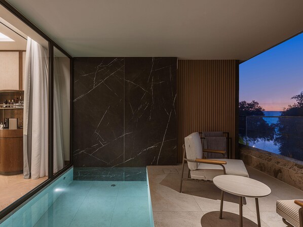 A modern bathroom with a marble wall, a bathtub, and a seating area with a view of the outdoors. - Hilton Chania Old Town Resort & Spa (Chania)