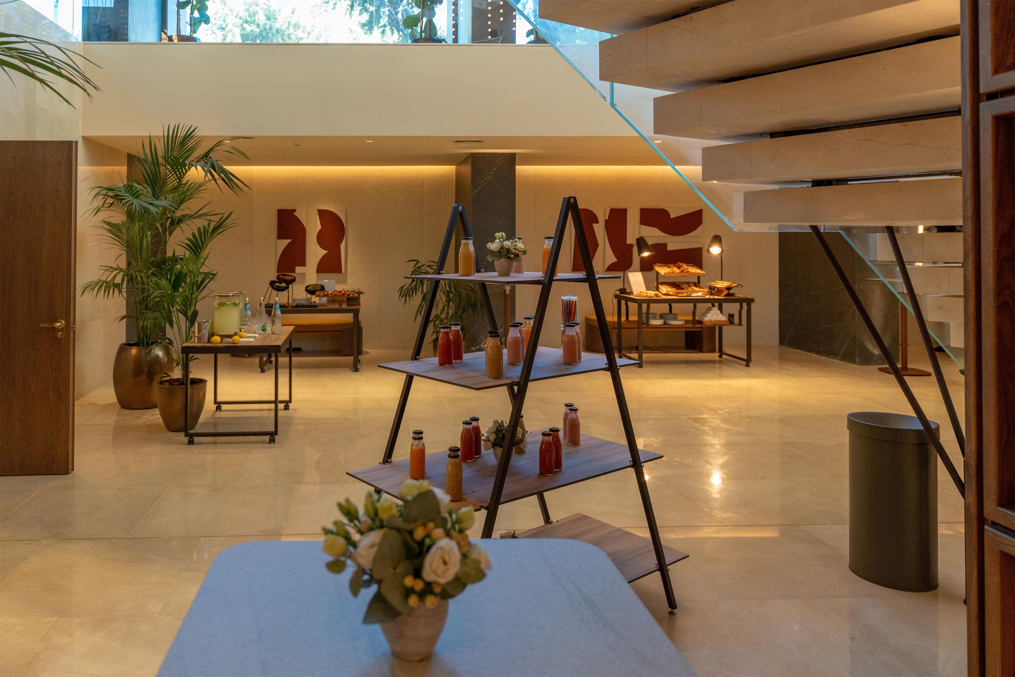 Un moderno vestíbulo de hotel con una mesa central que exhibe diversas bebidas, una escalera y una gran obra de arte abstracto en la pared.