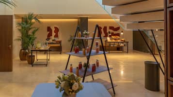 Un moderno vestíbulo de hotel con una mesa central que exhibe diversas bebidas, una escalera y una gran obra de arte abstracto en la pared.