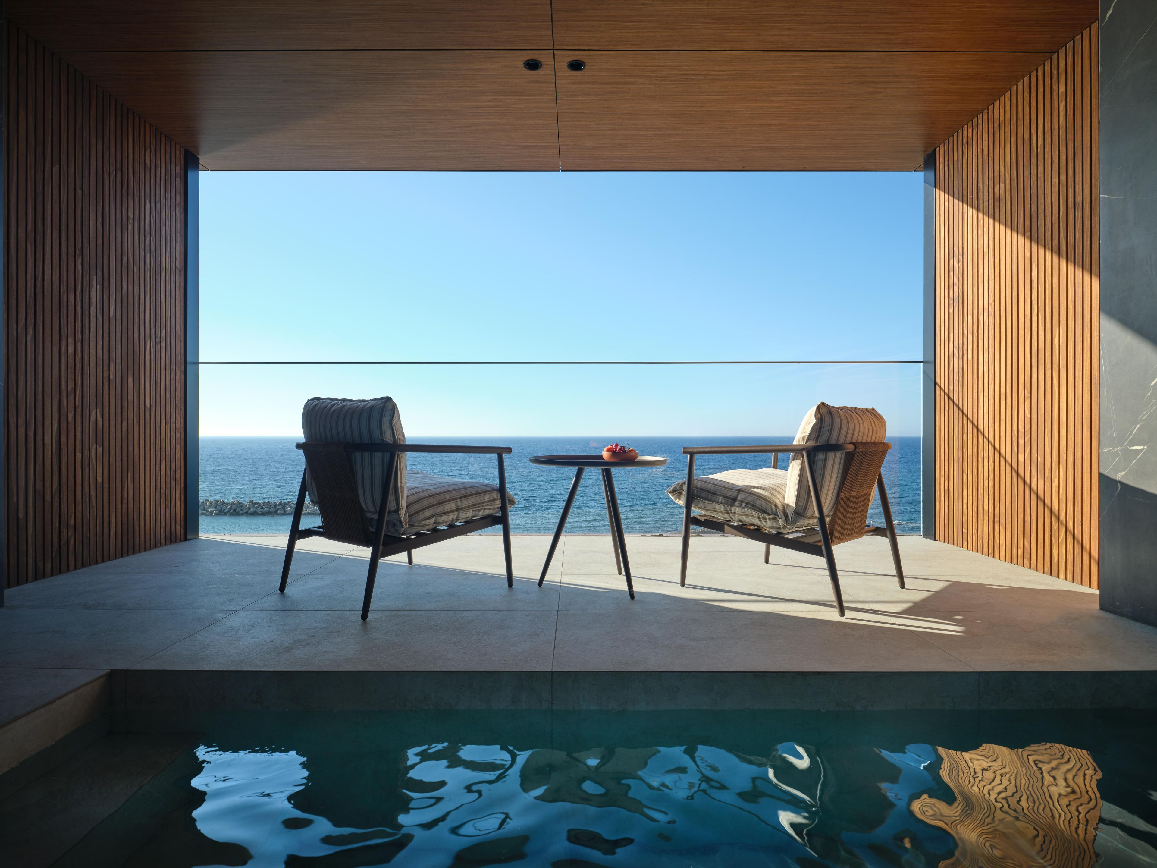 Una habitación moderna con piscina, dos sillas y una mesa con vista al océano.
