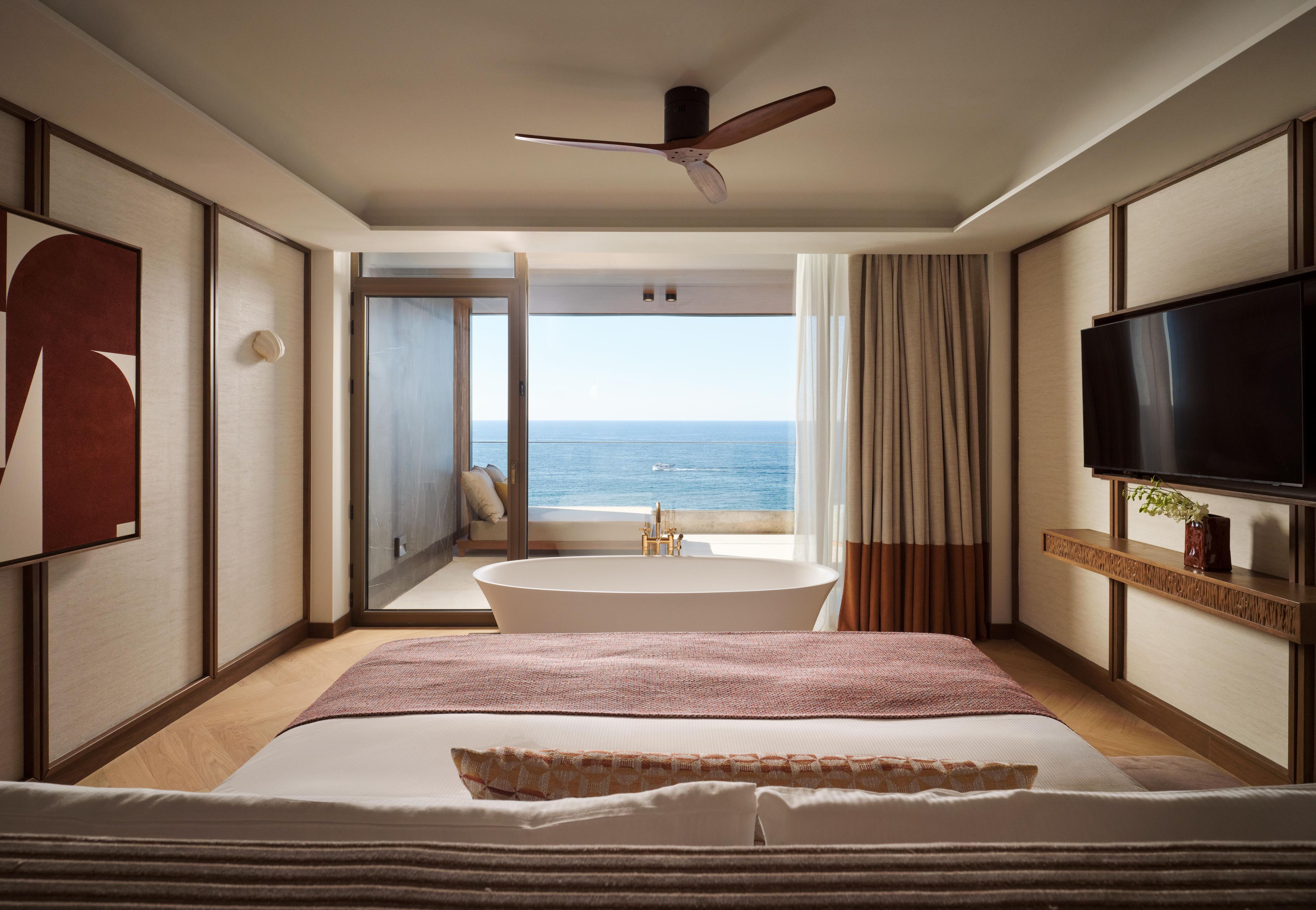 Een hotelkamer met een groot bed, een badkuip, een televisie en uitzicht op de oceaan.