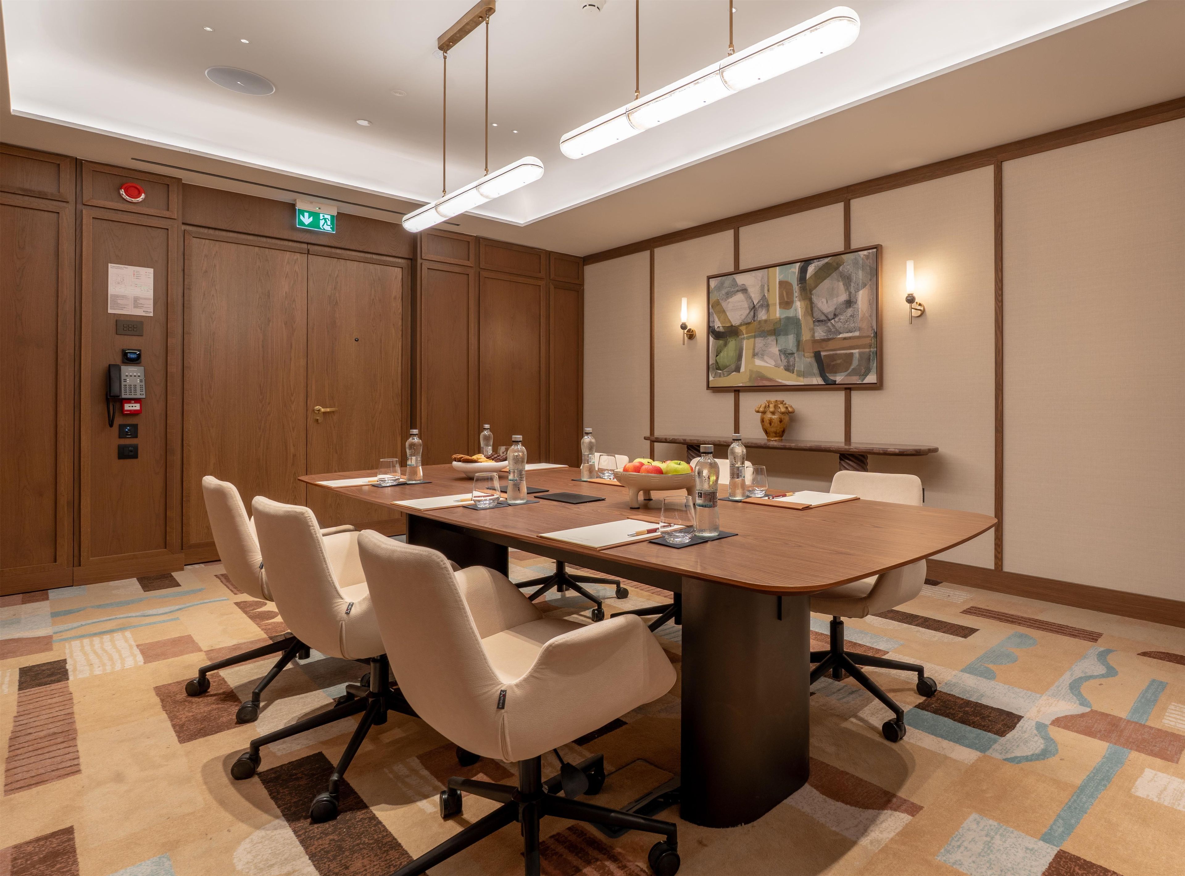A conference room with a long table, chairs, a phone, and a wall-mounted painting.