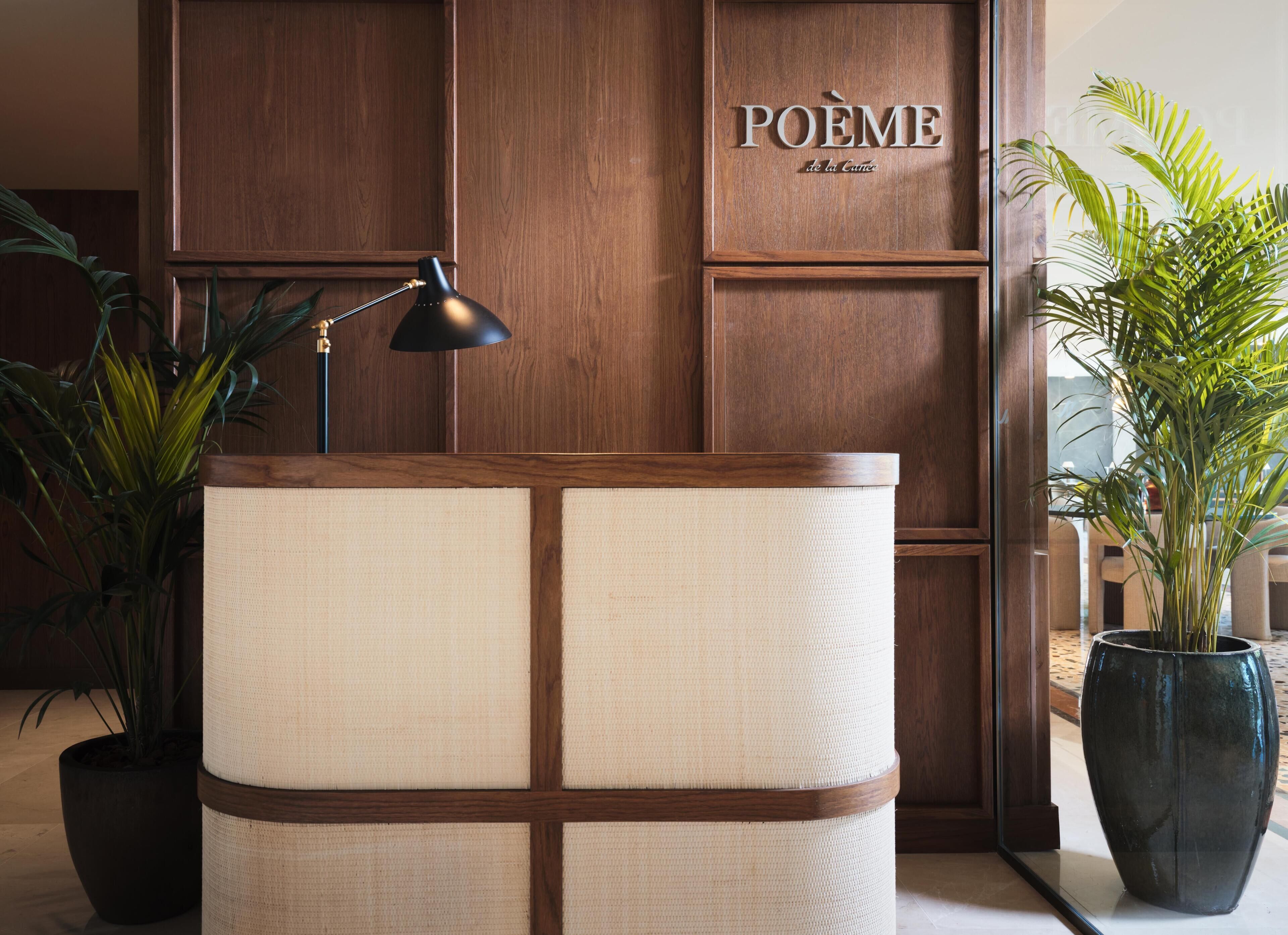 A reception desk with a woven chair, a lamp, and a potted plant.