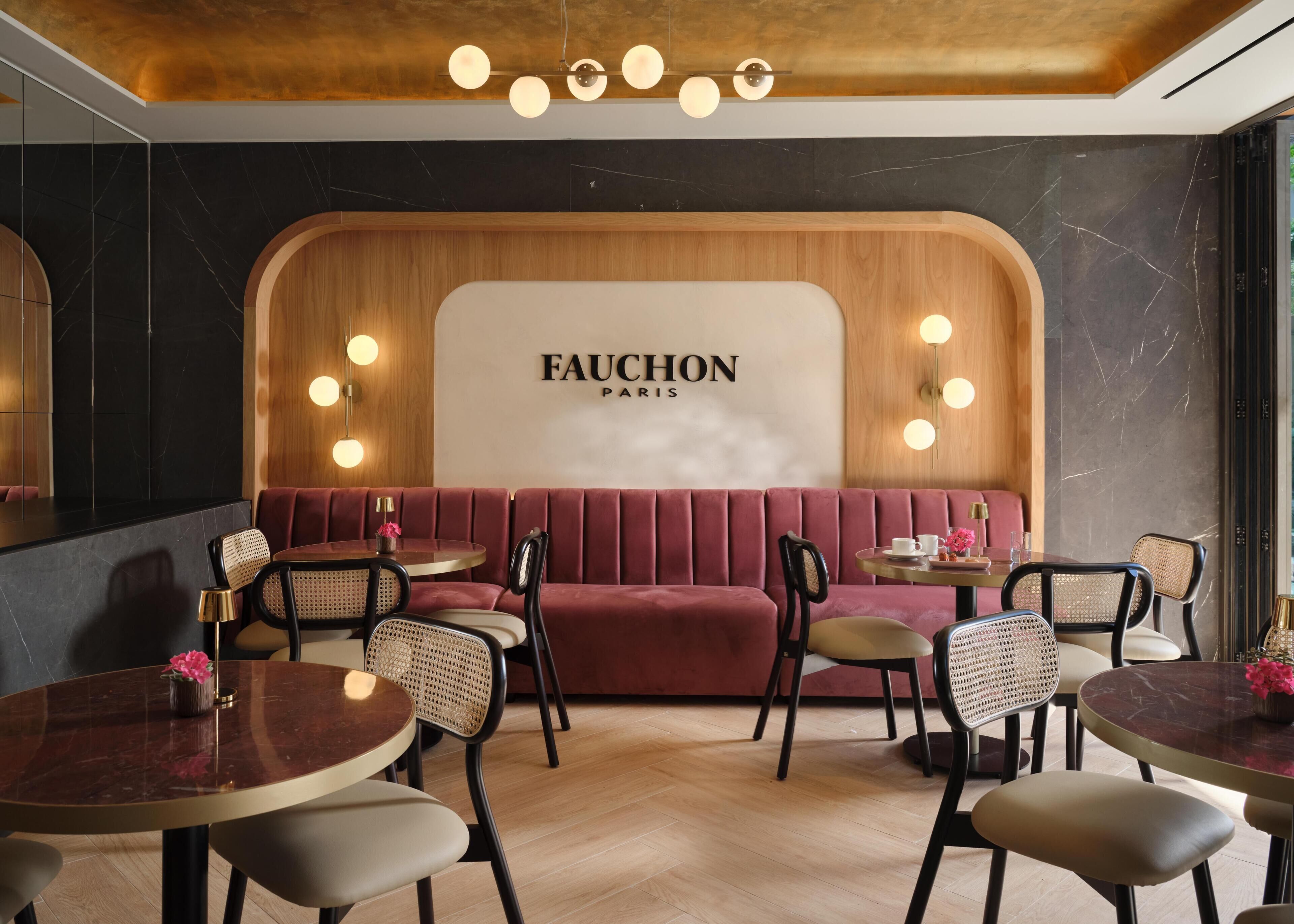 Een restaurantinterieur met een rode bekleden zitbank, ronde tafels en stoelen met geweven zittingen.