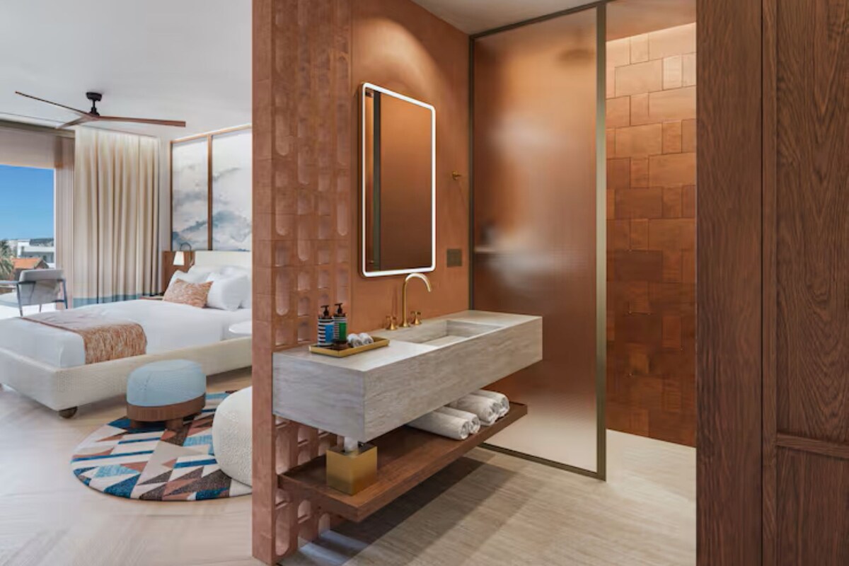 Ein modernes Hotelzimmer mit einem großen Bett, einem integrierten Schminktisch mit Spiegel und Blick auf die Stadt.