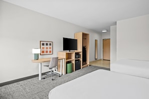 Quarto de hotel com cama, escrivaninha e cadeira, televisão, guarda-roupa e um pequeno cesto de lixo.