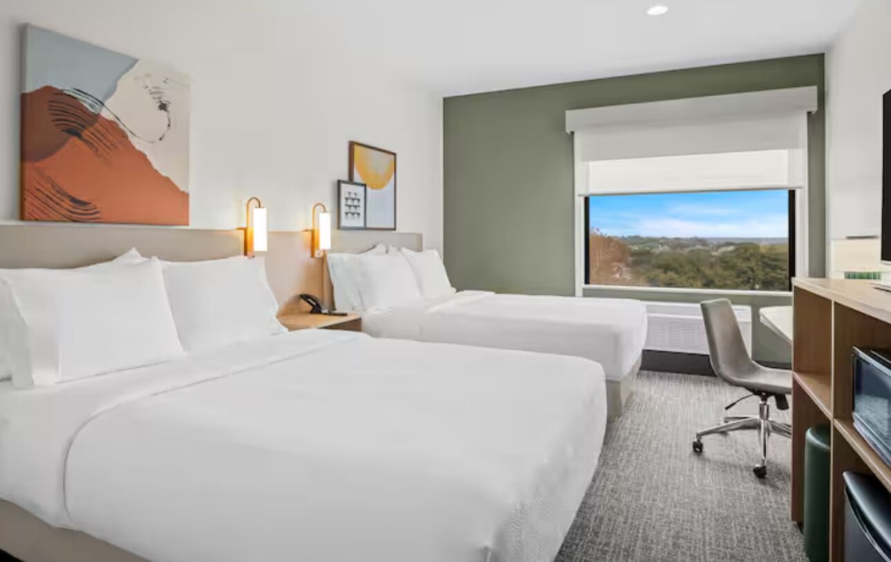 Une chambre d’hôtel avec deux lits, un bureau, une chaise, une télévision et une fenêtre donnant sur un paysage agréable.