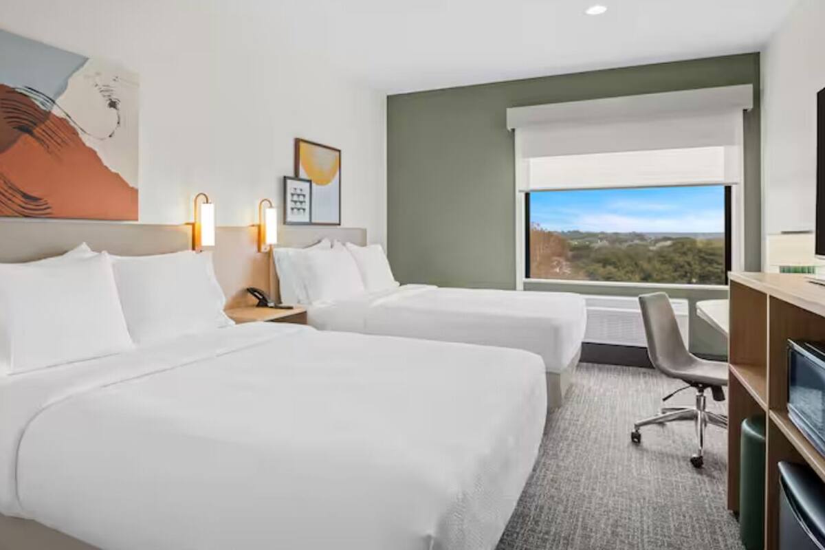 Ein Hotelzimmer mit zwei Betten, einem Schreibtisch, einem Stuhl, einem Fernseher und einem Fenster mit Blick.