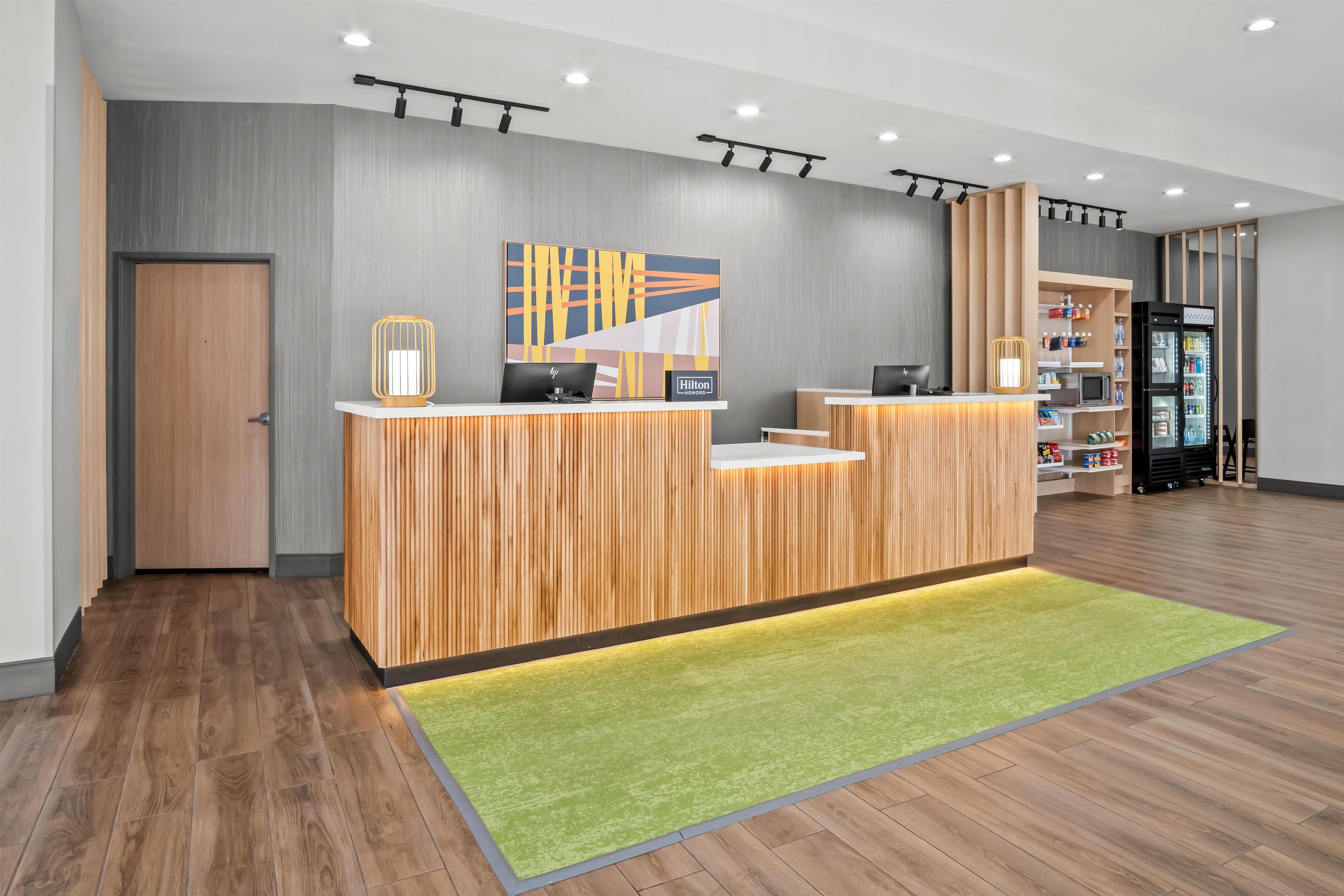A hotel reception desk with a modern design, a green carpet, and a wall-mounted artwork.