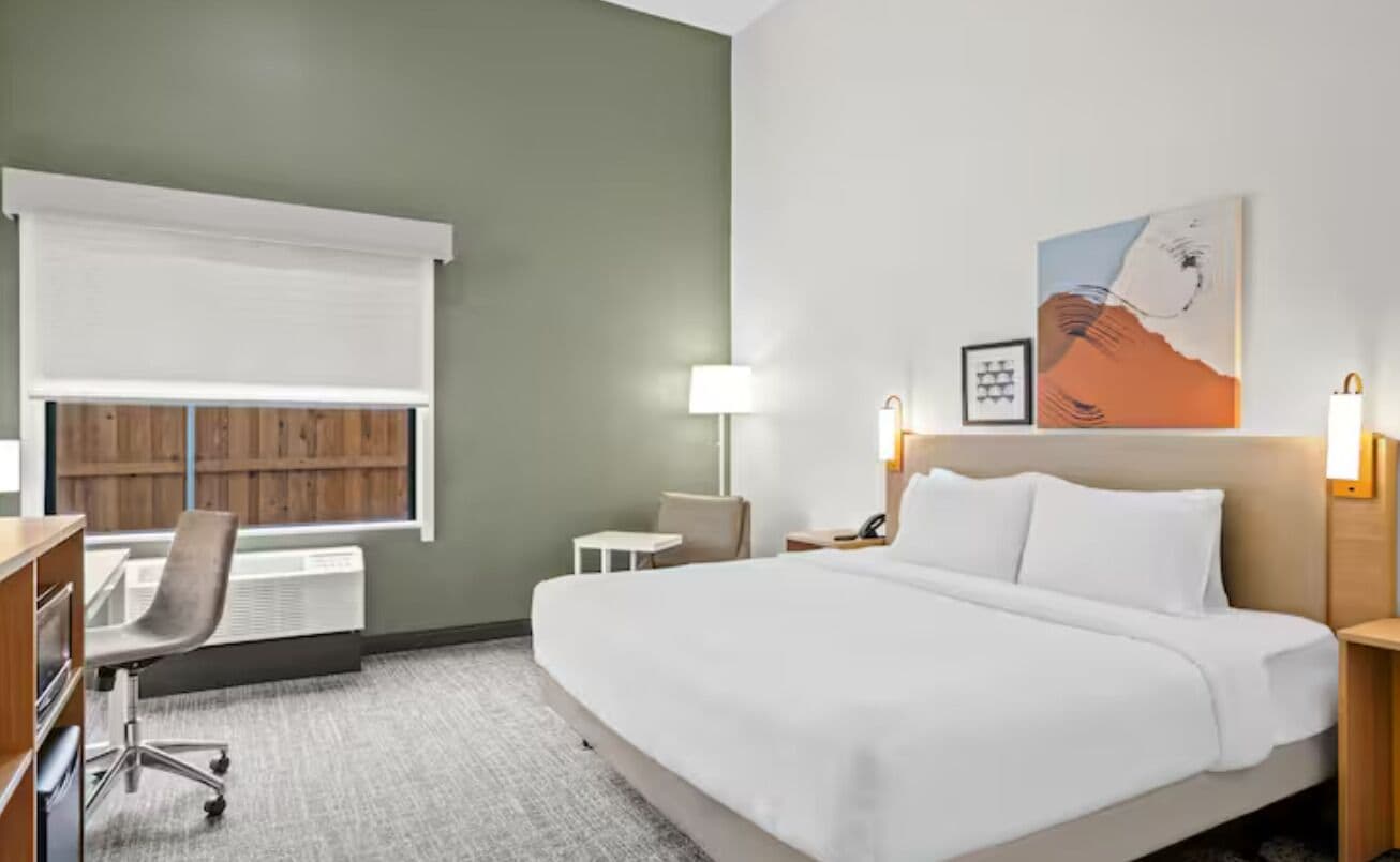 Une chambre d’hôtel équipée d’un lit, d’un bureau, d’une chaise, d’une lampe et d’une œuvre d’art au mur.