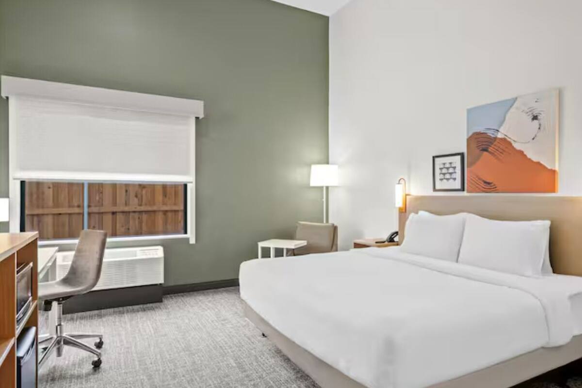 Ein Hotelzimmer mit Bett, Schreibtisch, Stuhl, Lampe und einem Kunstwerk an der Wand.