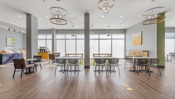 Un vaste espace dédié à la salle à manger, avec de nombreuses tables et chaises, de grandes fenêtres et un éclairage moderne suspendu au plafond.