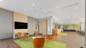 Un salon spacieux et moderne, doté d’un téléviseur à écran plat fixé au mur, d’un parquet et de fauteuils à bascule orange avec des coussins bleus.