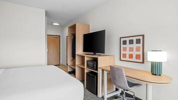 A hotel room with a bed, a desk with a chair, a television, a microwave, and a framed picture on the wall.