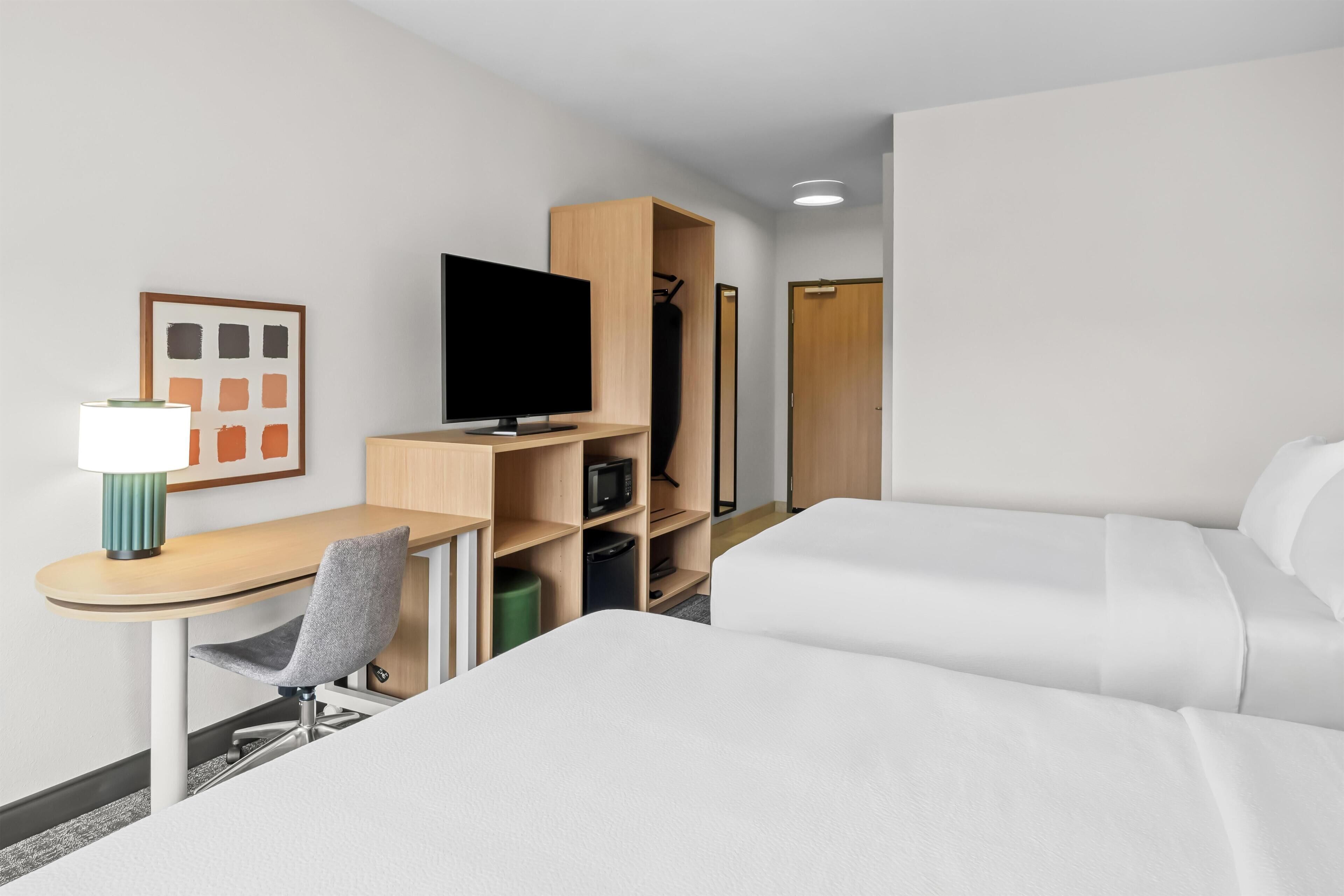 Une chambre d’hôtel comprenant un lit, un bureau avec une chaise, une télévision, une armoire et un tableau encadré au mur.