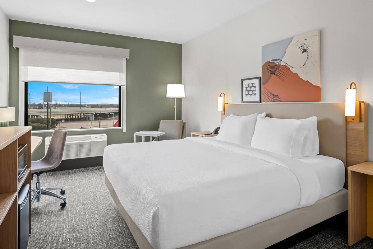 Ein Hotelzimmer mit einem großen Bett, einem Schreibtisch, einem Stuhl und Blick auf eine Brücke.