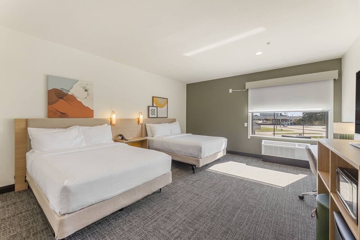 Ein Hotelzimmer mit zwei Betten, einem großen Fenster mit Blick, einem Schreibtisch mit Stuhl und einem Fernseher.