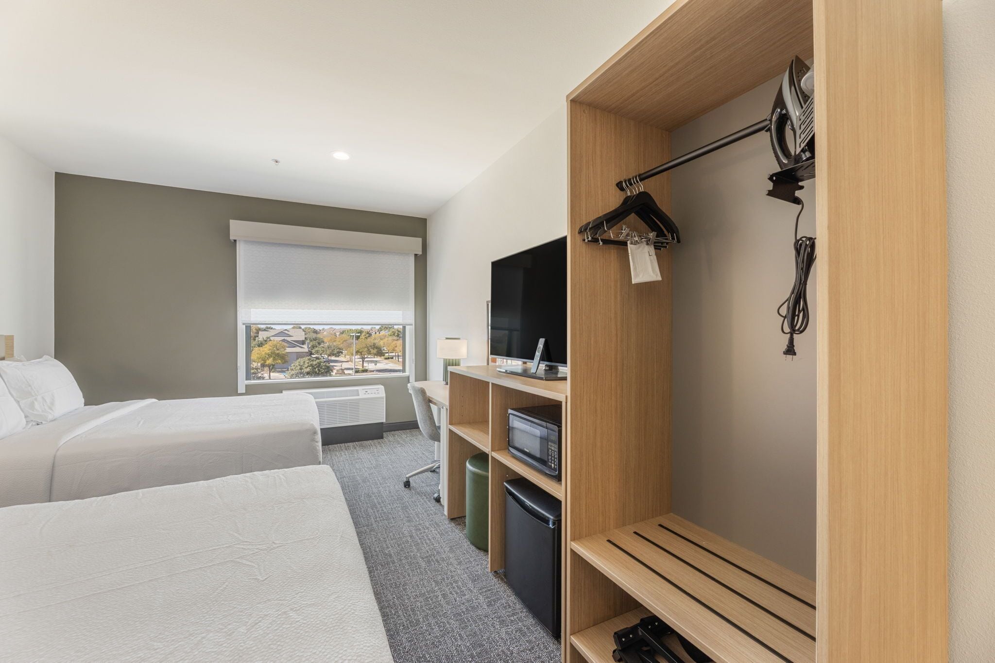 Ein Hotelzimmer mit zwei Betten, einem Schreibtisch, einem Fernseher und einem Kleiderschrank.