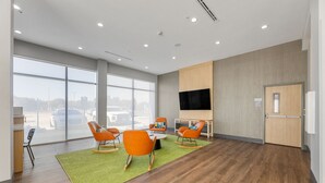 Une pièce spacieuse dotée de grandes fenêtres, d’un téléviseur à écran plat et de fauteuils orange.
