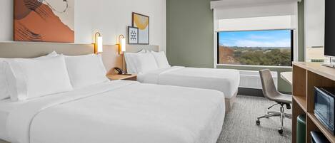 A hotel room with two beds, a desk, a TV, and a large window with a city view.