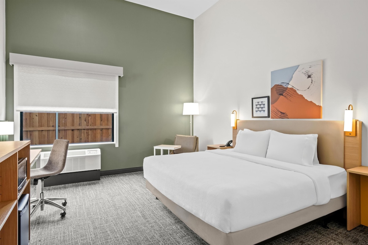 Une chambre d’hôtel avec un lit, un bureau, une chaise, une lampe et un tableau au mur.