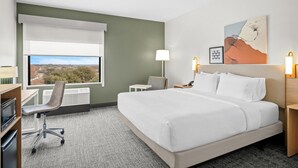 Une chambre d’hôtel avec un lit, un bureau, une chaise, une lampe et un tableau au mur.