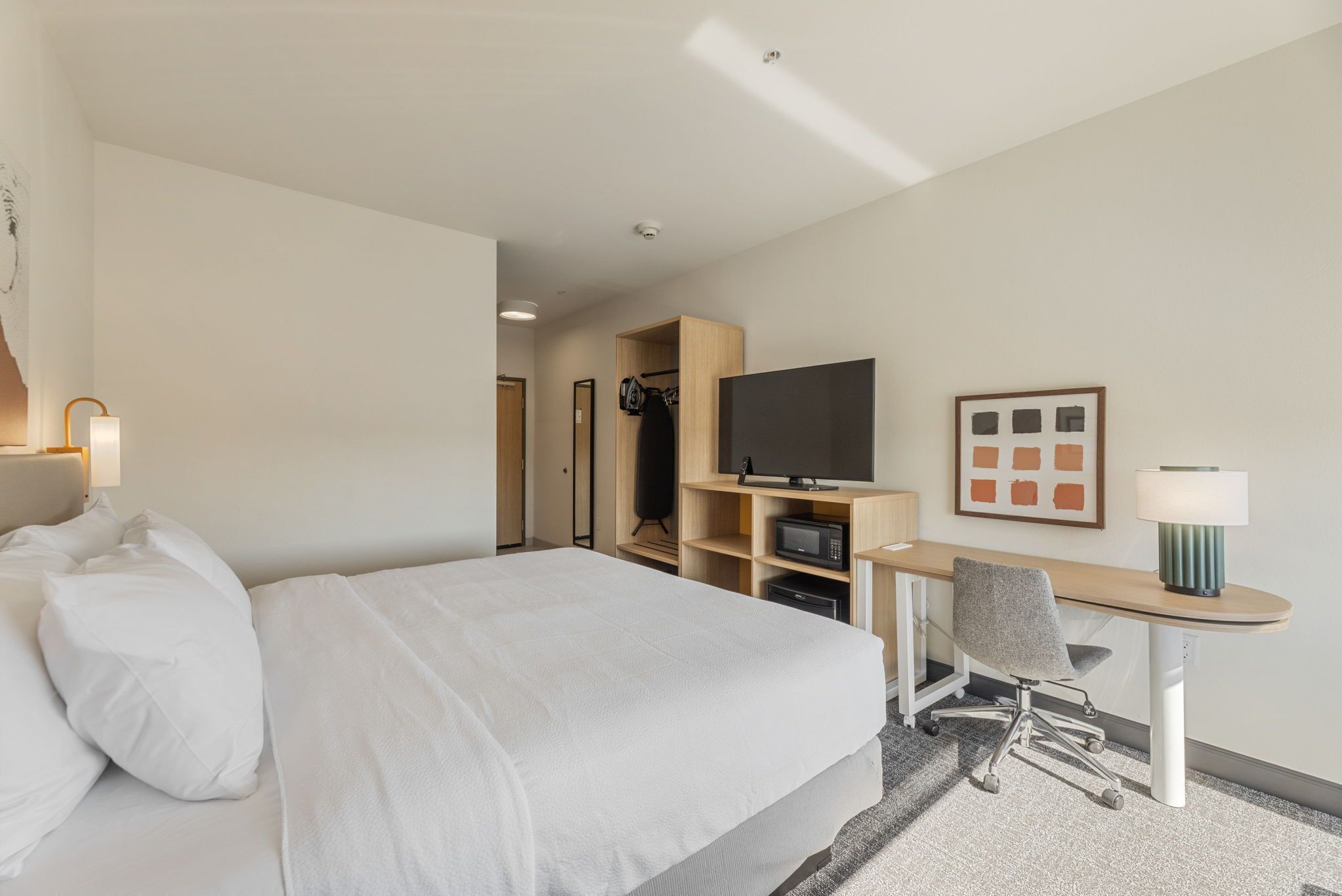 A hotel room with a large bed, a desk with a chair, a television, and a wardrobe.