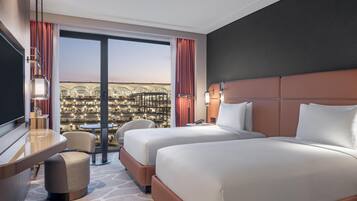 Quarto de hotel com duas camas, uma escrivaninha, uma cadeira e vista para a cidade.