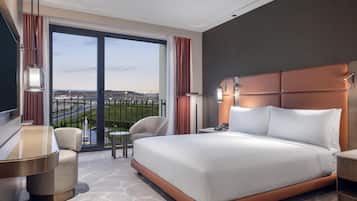 A hotel room with a large bed, a desk, a chair, and a view of the airport.