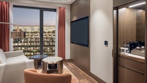 Habitació d'hotel amb finestra gran, televisió de pantalla plana, sofà, màquina de cafè i taula petita.