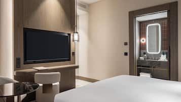 A hotel room with a bed, a desk, a chair, a television, and a bathroom with a mirror.