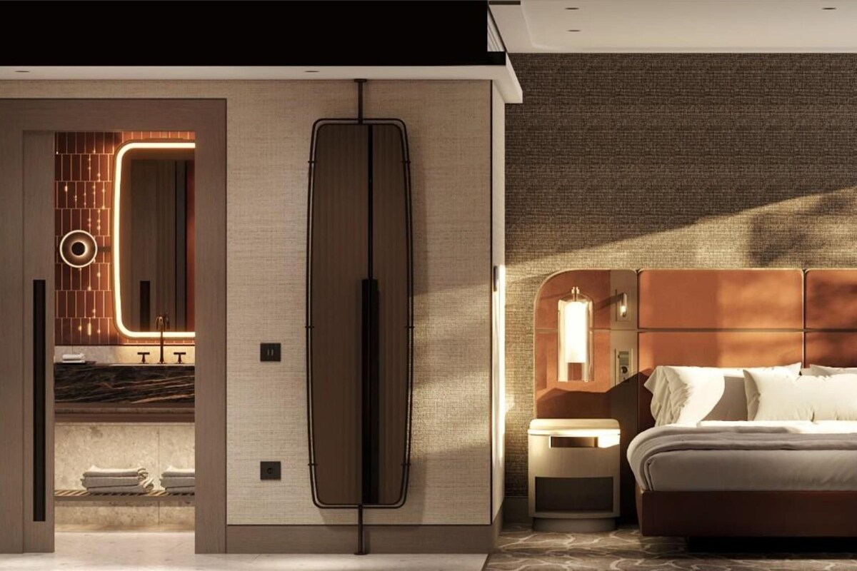 A modern hotel room with a large bed, bedside tables, a seating area, and a bathroom with a vanity and towel rack.