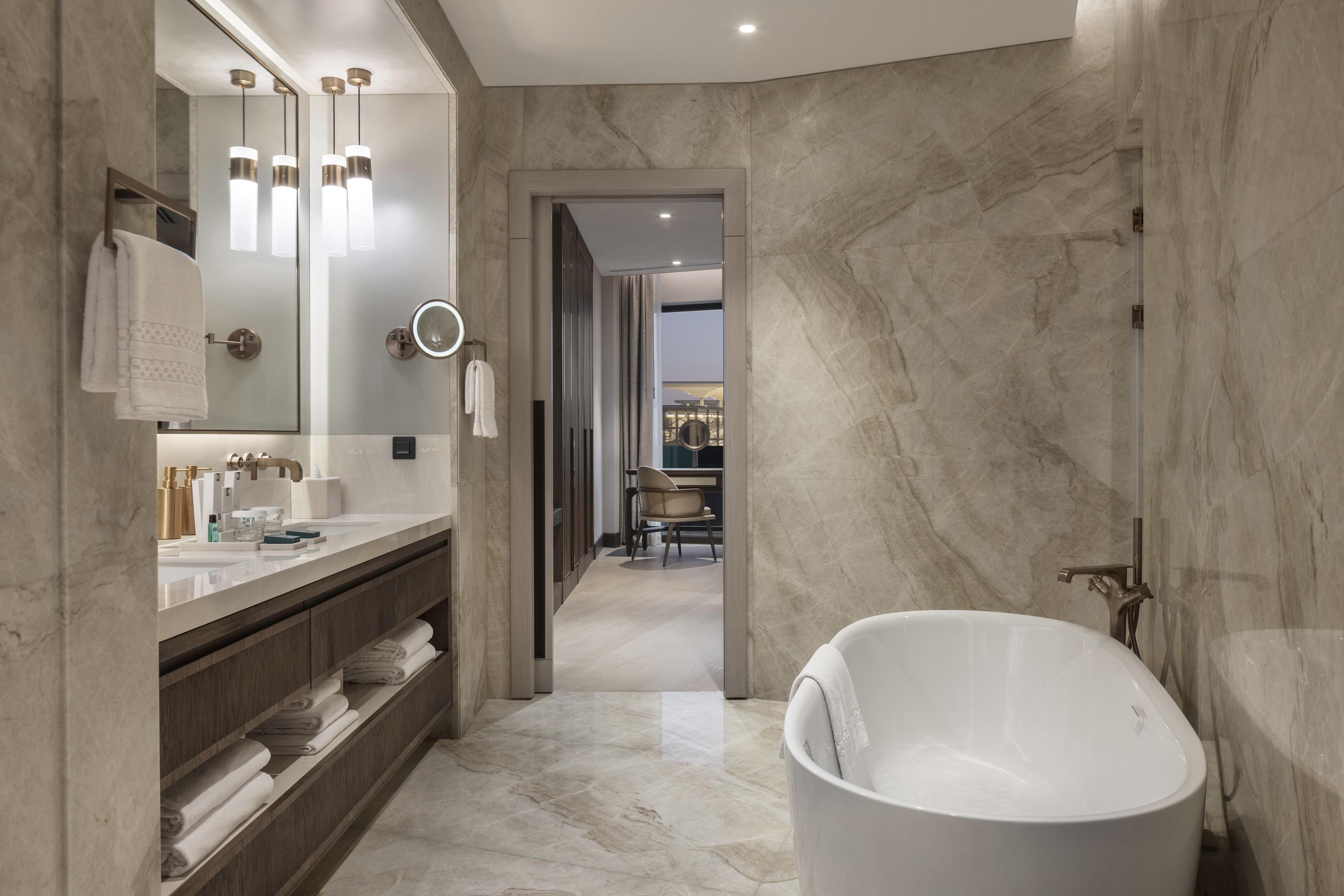 Ein modernes Badezimmer mit einer freistehenden Badewanne, einem Waschtisch mit Spiegel und Beleuchtung sowie Marmorwänden.