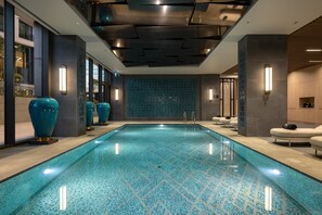 A modern indoor swimming pool with a blue mosaic tile floor, surrounded by spa facilities and large decorative vases. - Hilton Istanbul Airport (Arnavutköy)