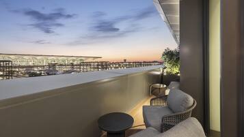 A balcony with a view of a modern building complex, a small round table, and two cushioned chairs.