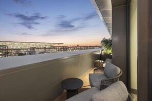 A balcony with a view of a modern building complex, a small round table, and two cushioned chairs. - Hilton Istanbul Airport (Arnavutköy)