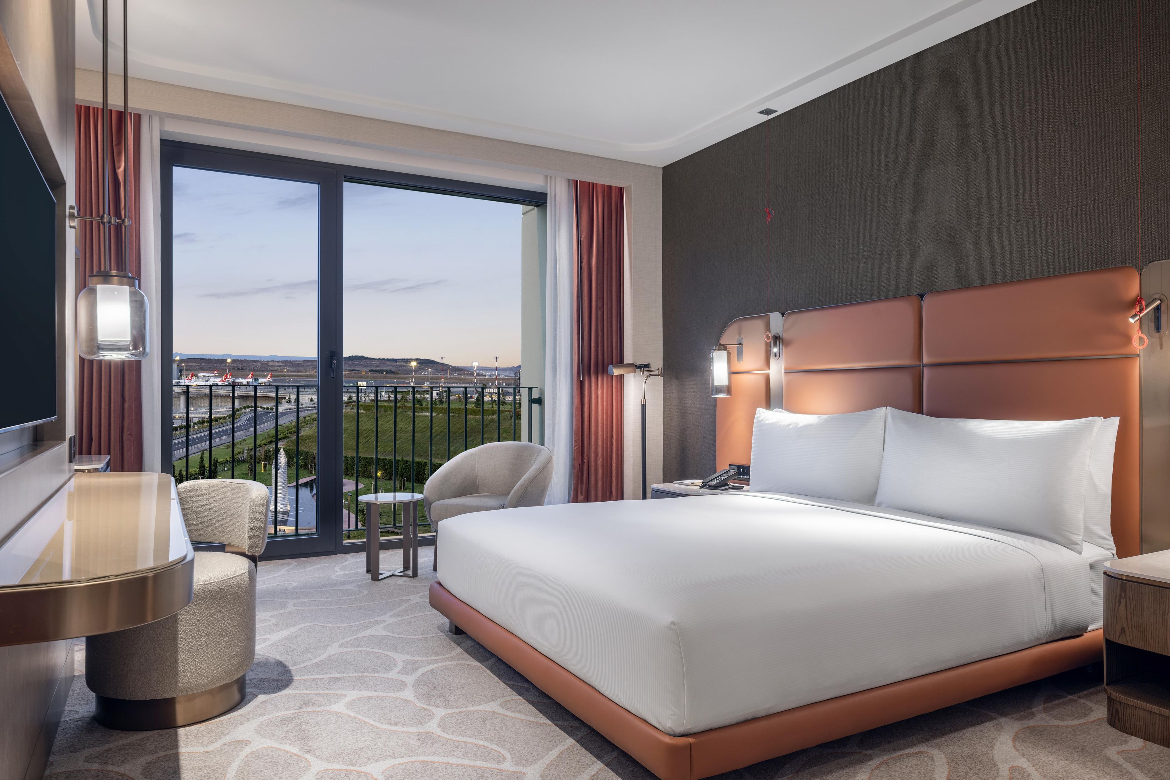 Camera d'albergo con un letto grande, una scrivania, una sedia e vista sull'aeroporto.