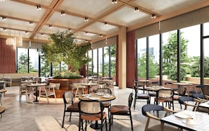 A spacious indoor dining area with multiple tables and chairs, large windows offering a view of the city, and a central plant. - Hilton Istanbul Airport (Arnavutköy)