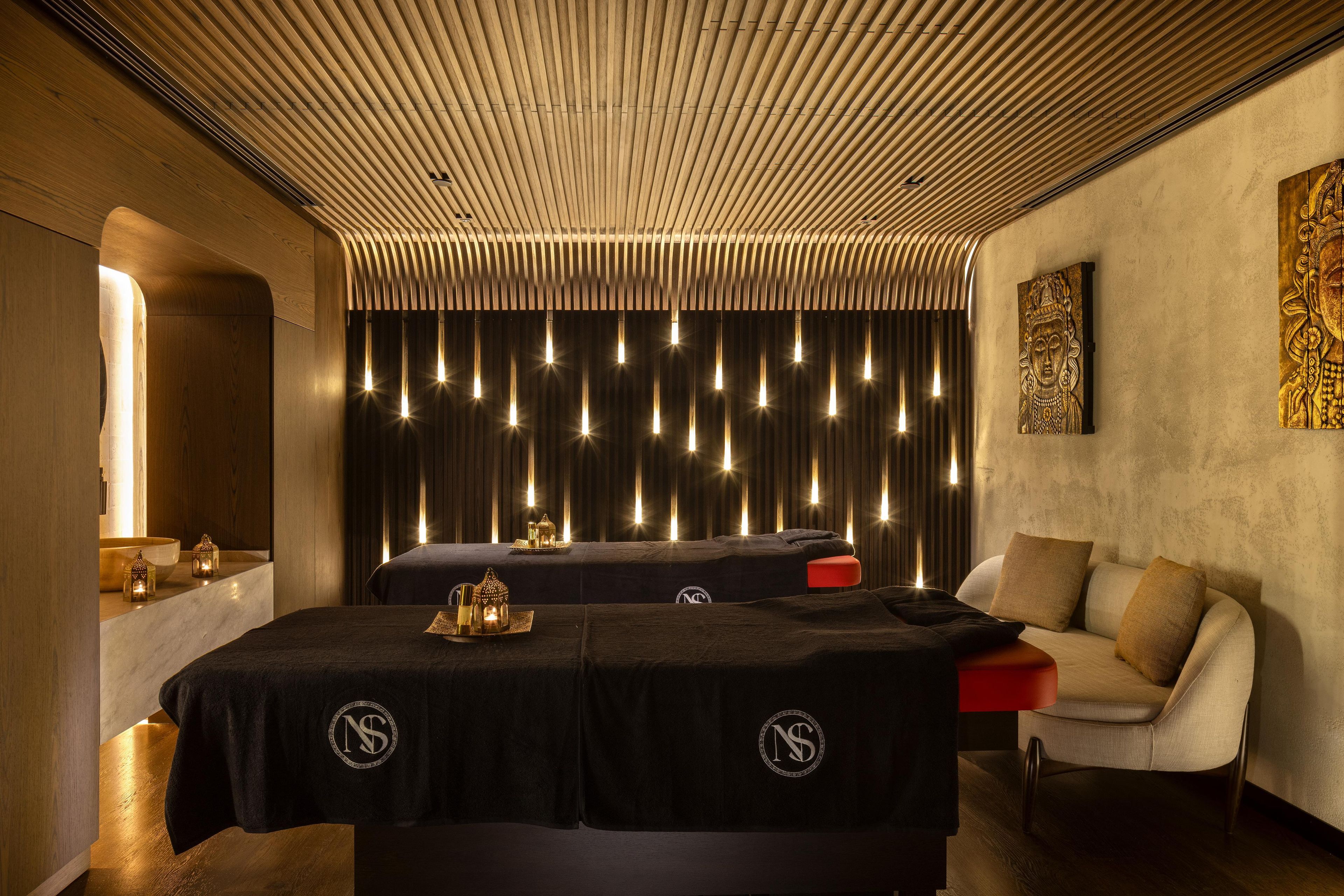 Een moderne spa ruimte met een houten plafond, een massagetafel, een massagestoel en een kunstwerk aan de muur.